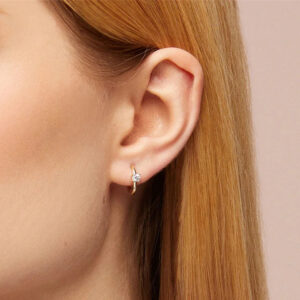 Gold huggie hoop earrings close-up worn on earlobe profile view small CZ accent