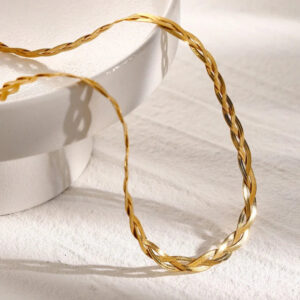 Close-up detail of 18K gold braided necklace showcasing shiny polished twisted woven flat chain texture, displayed on ceramic prop with linen fabric backdrop