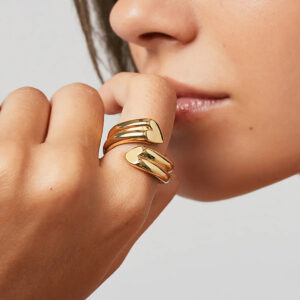 Female model wearing 18K gold heart twist rings on fingers close-up hand shot near face showing versatile stacking capability