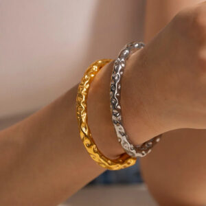 Woman wearing two hammered gold and silver open cuff bracelets stacked on wrist close-up detail shot