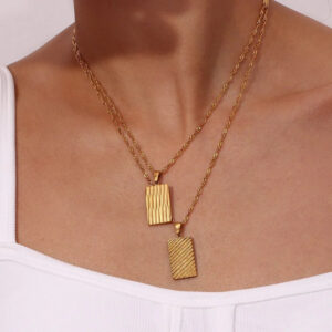 Layered double 18K gold dahlia necklaces worn on model, close-up neck shot showing dual geometric striped pendants