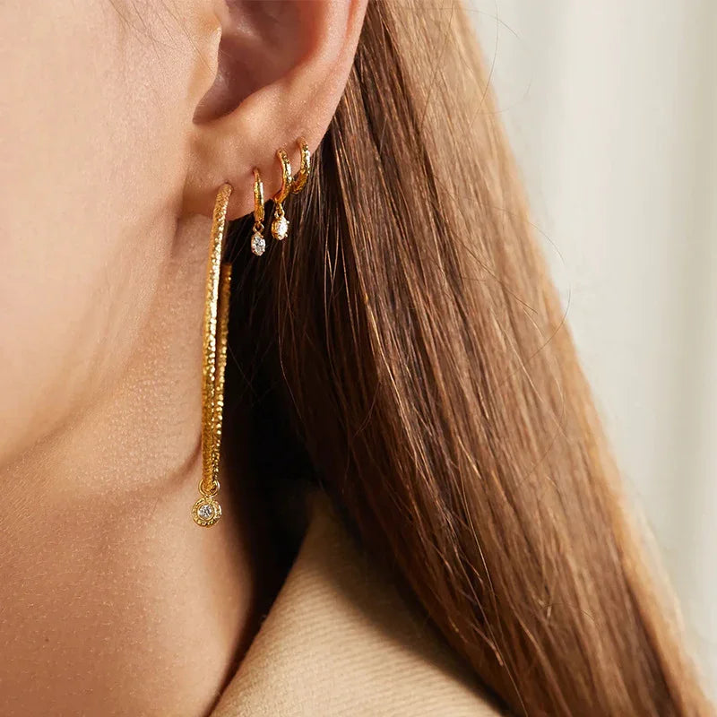 Close-up styling view showing 18K gold hammered chain drop earring paired with small diamond huggie hoops worn together on model