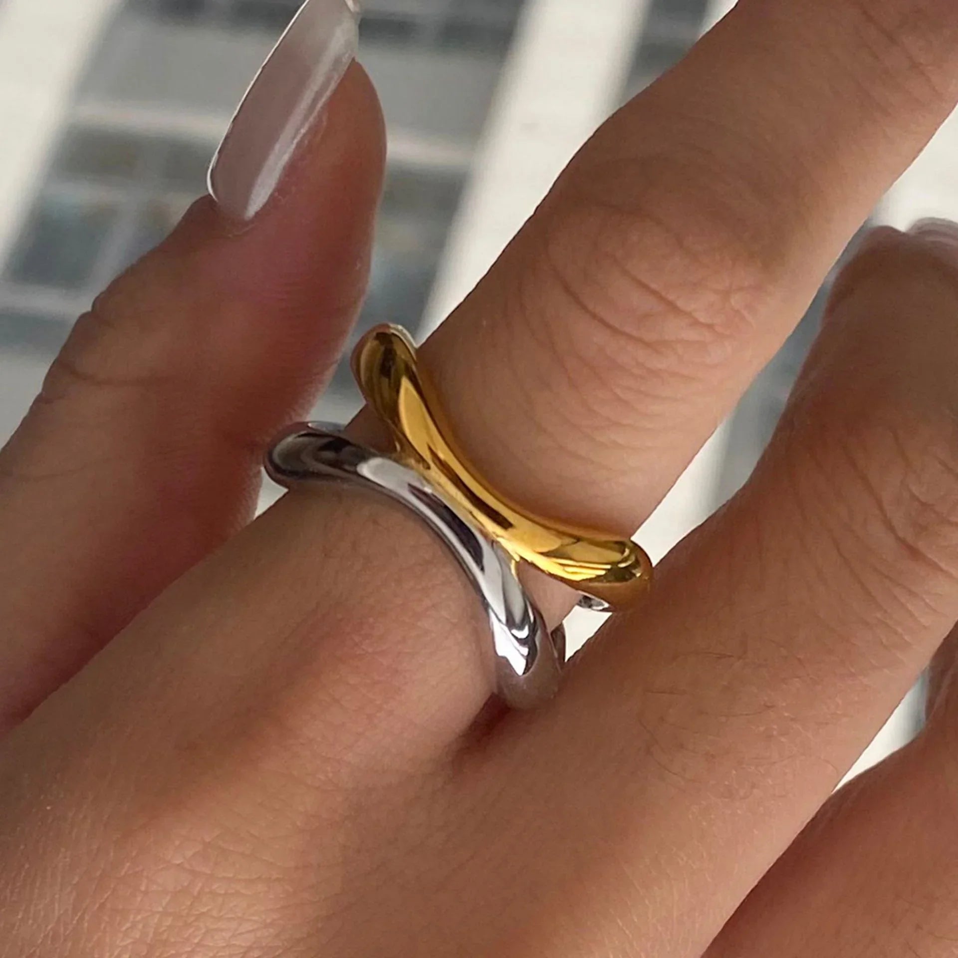 Two-tone gold and silver intertwined ring worn on female hand with long nails, close-up detail shot