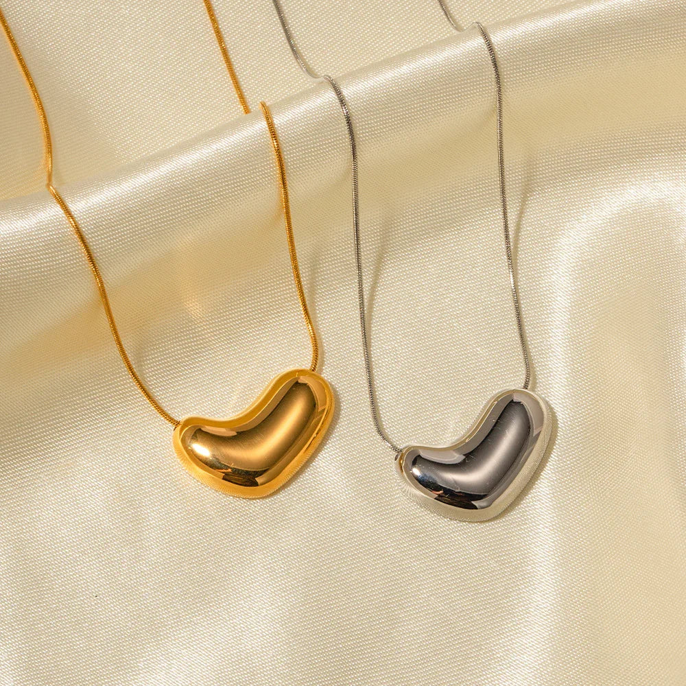 gold and silver bean pendant necklaces side view flat lay beige silk fabric background matching pair