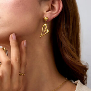 18K gold heart dangle earrings worn by woman, side close-up detail showing sleek shiny gold metal and secure ear post