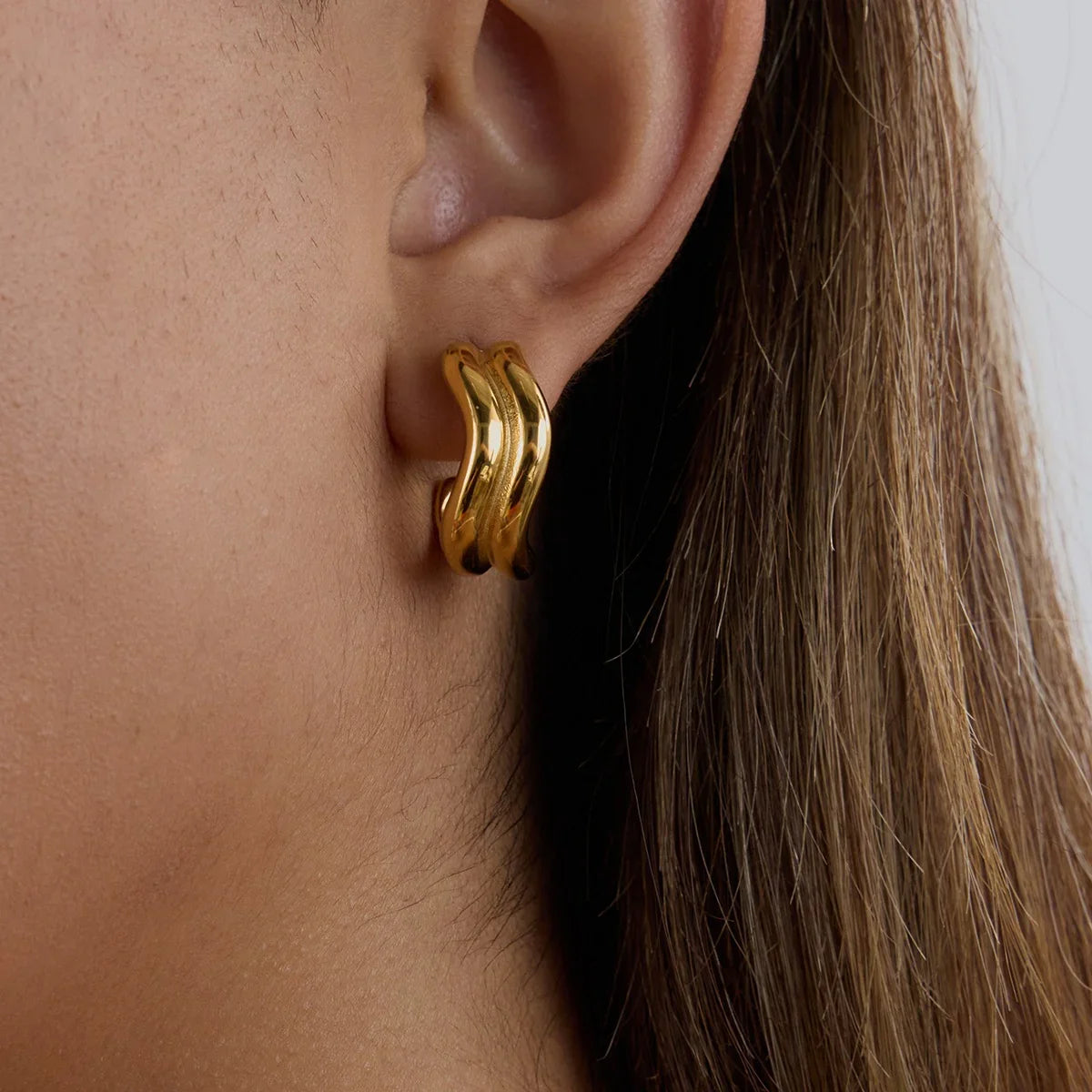 18K gold double-curve hoops on female ear, earlobe close-up, polished yellow gold, refined elegance