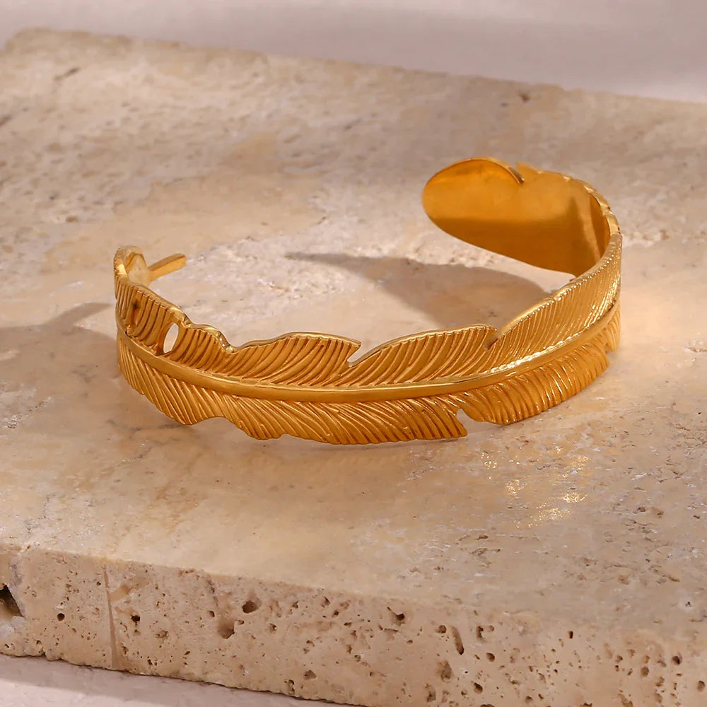 18K gold feather shaped open cuff bracelet full front view with carved feather veins bright gold finish on beige stone