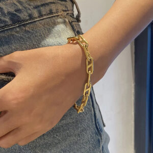 Gold chain bracelet worn on female wrist with denim jeans, close-up side view showing polished gold tone and bold chain design in everyday casual style