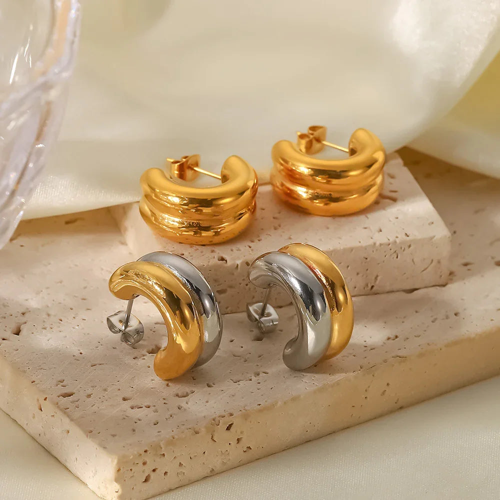 Mixed style 18K gold and two-tone hoop earrings on travertine stone and satin fabric display surface