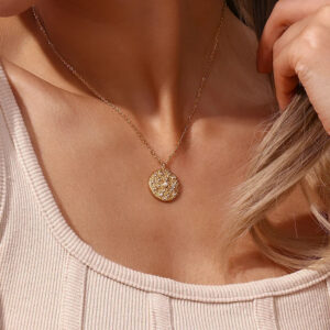 Close-up of delicate 18K gold necklace worn on female model, compact disc pendant at collarbone, light pink ribbed top