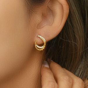 Gold crescent hoop earrings worn on woman's ear, showcasing beaded edges and crystal inlay details, close-up side profile