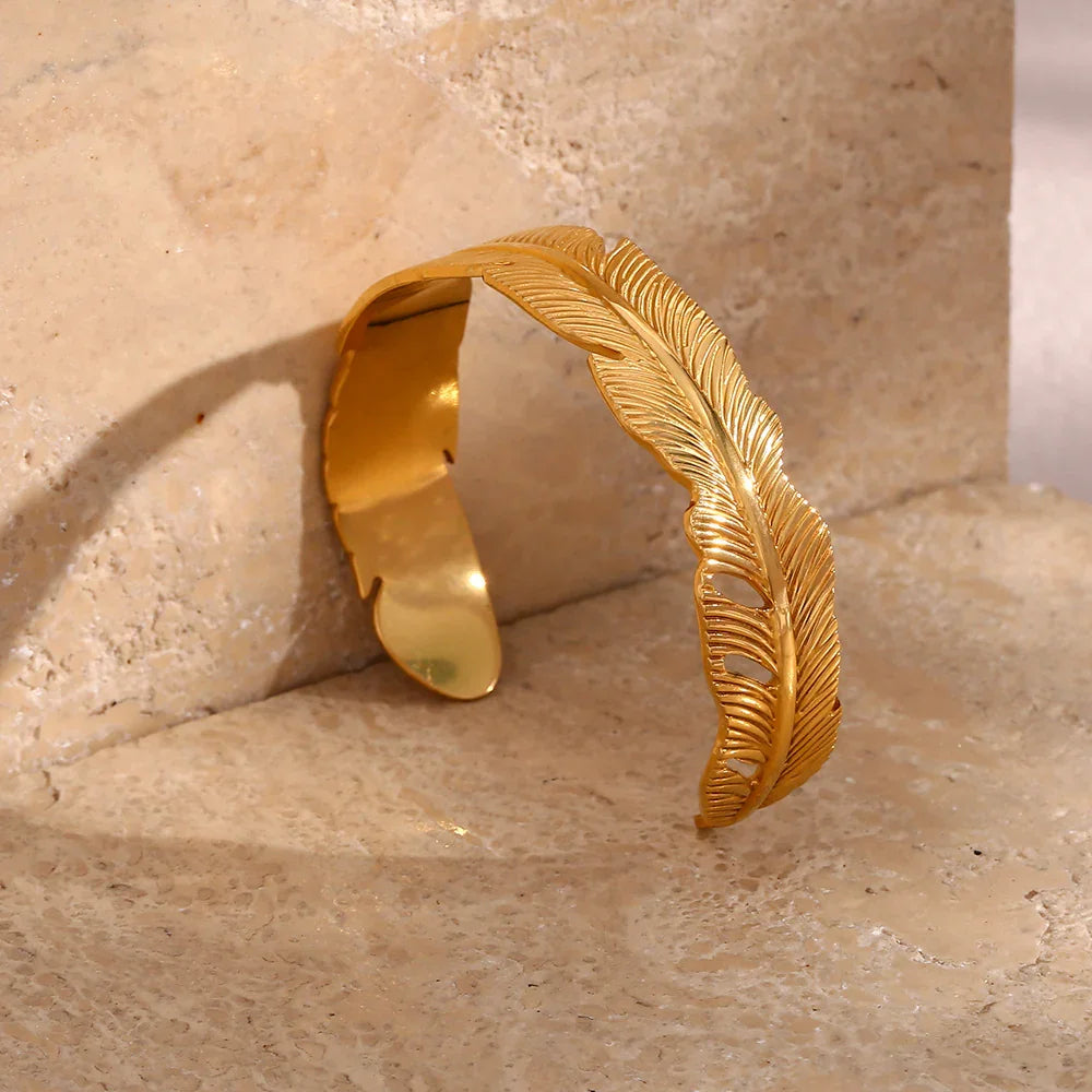 18K gold feather cuff bracelet back view showing open design and feather vein details on stone background