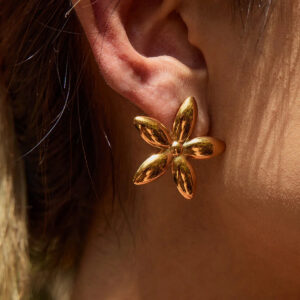 Woman wearing 18K gold flower stud earrings, close-up side ear view showing floral design on brown hair