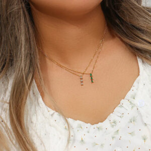 Woman wearing dual-layered 18K gold necklace with teardrop diamond simulant pendants and green stone accent close-up neck shot lifestyle