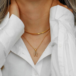 Stacked 18K gold initial necklaces worn on neck, close-up wearing white button-up shirt, personalized dual chain style