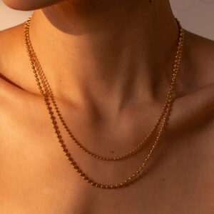Layered 18K gold ball chain necklace worn on woman's neck and collarbone showing how it drapes with golden beads close-up view