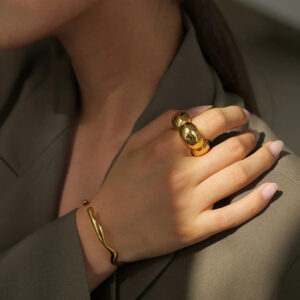 Chunky 18K gold curved band ring worn on female hand model in brown blazer, close-up detail shot showing polished luxury finish