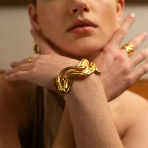 18K gold wavy bracelet worn on wrist with matching gold rings styled elegant close-up portrait