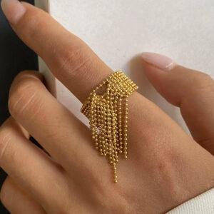Close-up side view of 18K gold tassel ring on finger with fringe pendant design