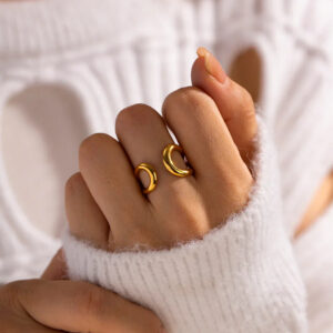 Woman wearing matching 18K gold twisted open rings on hand close-up side view, minimalist gold plated band ring stacked styling with white knit sweater