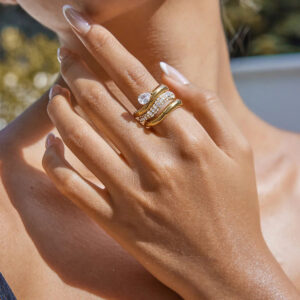 Close-up model hand wearing stacked 18K gold twisted rings with diamond accents outdoors