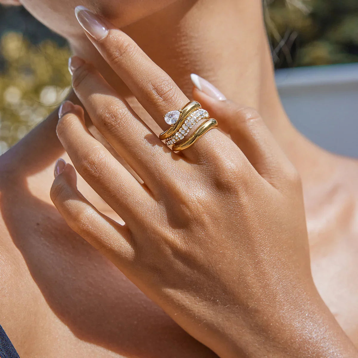 Close-up model hand wearing stacked 18K gold twisted rings with diamond accents outdoors