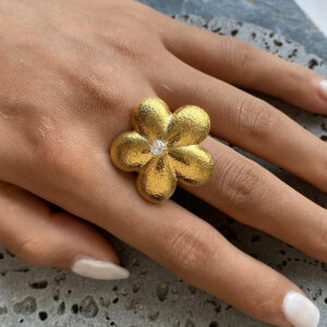 18K gold flower statement ring worn on female hand with white manicure, displaying five-petal botanical design and adjustable open ring band