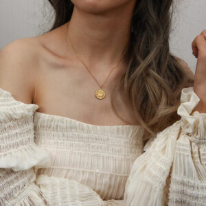 18K gold sun coin pendant necklace worn on model - dainty gold chain with small round sun pendant on off-shoulder neckline