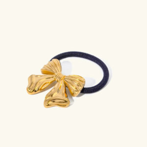 18K yellow gold bow hair cuff flat lay close-up, polished gold bow on black fabric hair ring against white background