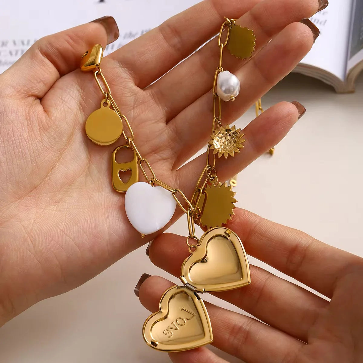 18K gold heart locket necklace with double engraved heart lockets and multiple gold charms, single hand holding product detail