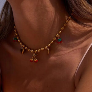 18K gold cherry charm choker necklace worn on model, close-up of neck showing delicate gold chain with red-green enamel cherry charms and heart details