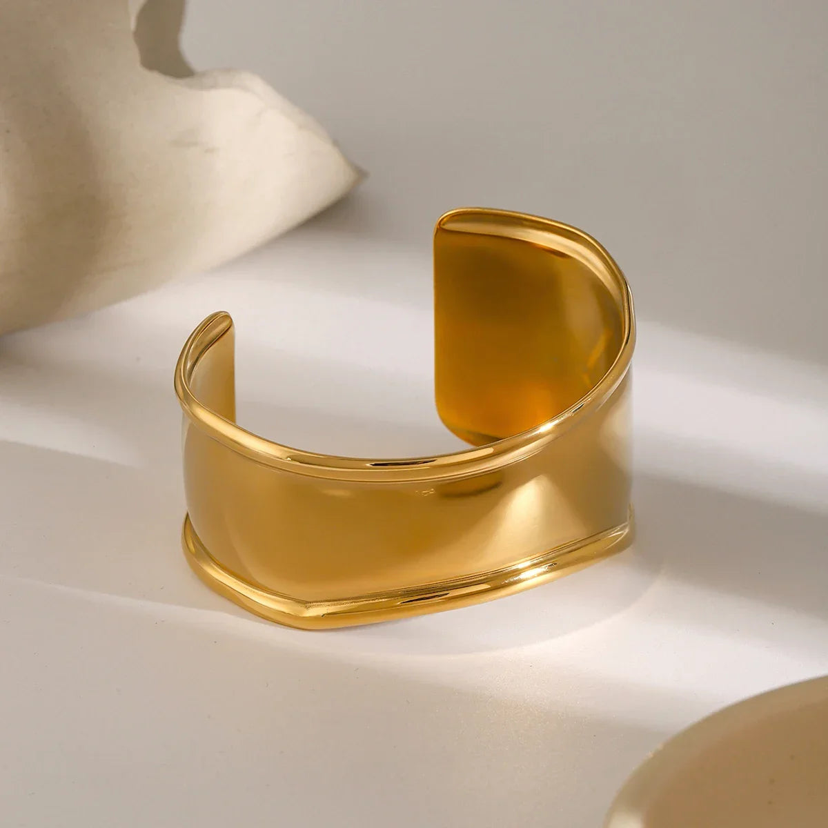 18K gold smooth cuff bracelet three-quarter overhead view with warm gold coloring and raised border detail, styled on ceramic tabletop decor