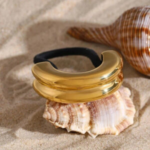 18K gold double arch pony cuff hair tie top-down close-up view with polished finish on beach sand background