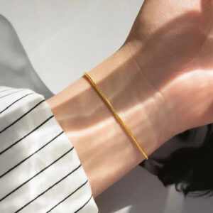 Delicate 18K gold thin snake chain bracelet worn on wrist with natural sunlight showing slim design