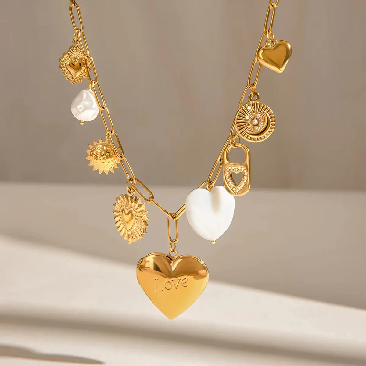 18K gold heart locket necklace studio flat lay with all charms visible, love engraved heart locket on neutral grey background
