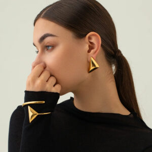 Woman wearing 18K gold geometric triangle earrings with matching coordinated gold cuff bracelet, side profile view, minimalist jewelry styling