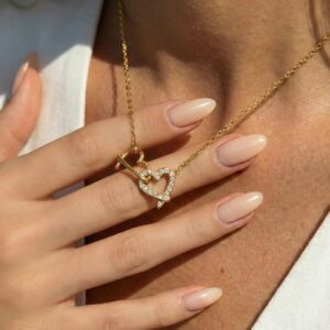 Close-up detail of crystal pavé heart pendant on delicate gold chain with hand and white clothing