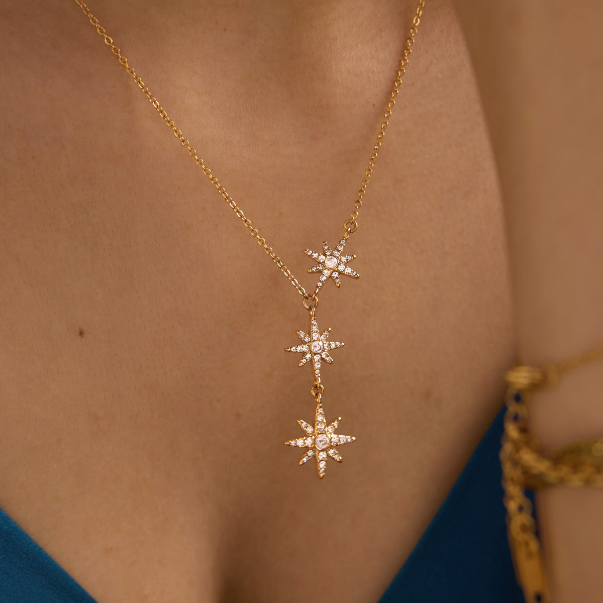 18K gold triple star cascade necklace overhead collarbone view on model wearing teal satin camisole with gold bracelet