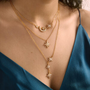 18K gold layered celestial necklace trio featuring cascade stars moon and star pendant with pavé diamond simulants worn on model collarbone close-up view
