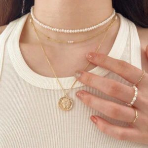 Dainty pearl and gold jewelry layering set with choker necklace, coin pendant, and stackable pearl rings worn by female model
