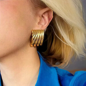 Chunky gold ribbed stud earrings worn on ear side profile close-up layered design