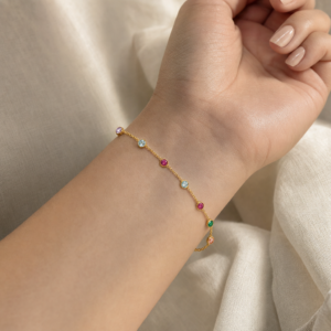 Dainty 18K gold gemstone bracelet close-up worn on light-skinned female wrist showing delicate thin cable chain with mixed round bezel-set colored stones