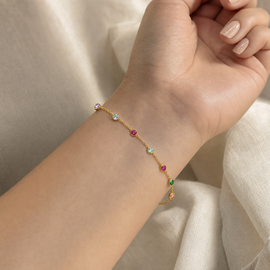 Dainty 18K gold gemstone bracelet close-up worn on light-skinned female wrist showing delicate thin cable chain with mixed round bezel-set colored stones