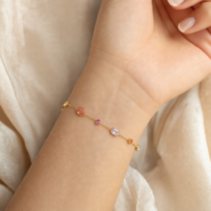 Dainty 18K gold colorful gemstone bracelet on wrist - close-up side view showing delicate bezel-set crystals and fine gold chain on light skin tone model
