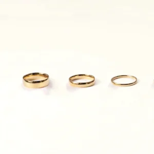 Three minimalist 14K gold band rings in varying widths displayed on white background flat lay - delicate 1mm, classic 3mm, and statement 6mm polished gold bands