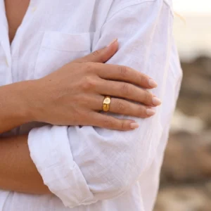 Close-up of delicate 14K gold band ring worn on female hand with white linen shirt - minimalist polished gold ring styling