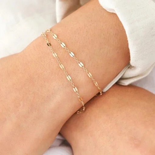 Layered gold chain bracelets stacked on female wrist in casual home setting, demonstrating versatile stacking style options