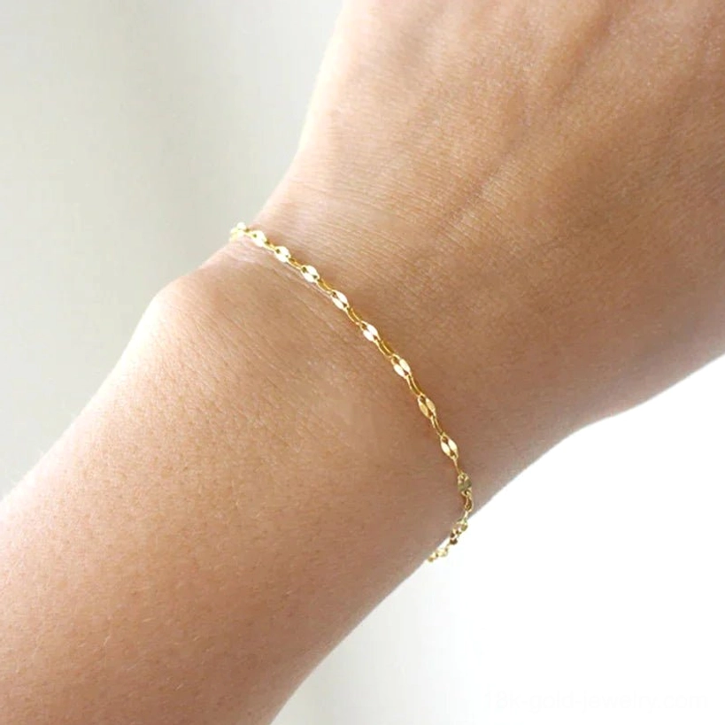 Gold chain bracelet fitted on bare female wrist in close-up, showing shiny flat link design and comfortable wear fit