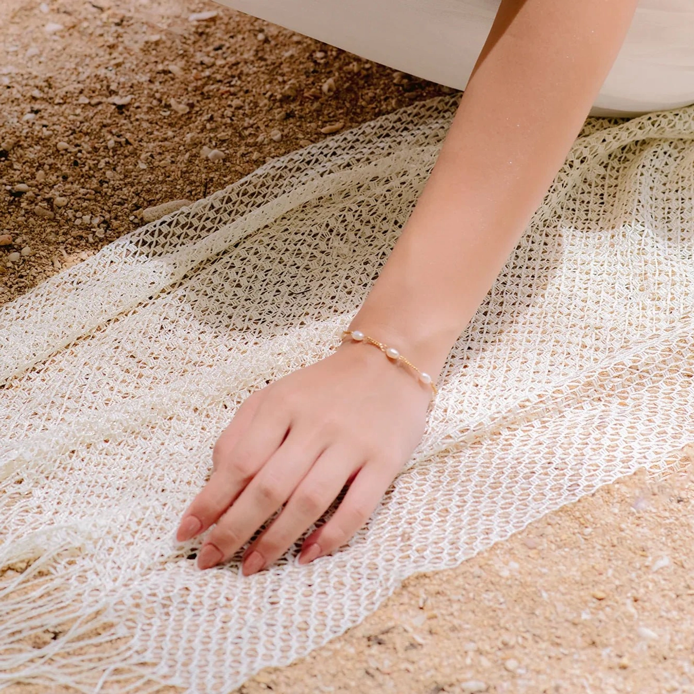 14K gold pearl bracelet worn on female wrist styled on beach sand and knit fabric showing delicate pearl cluster and gold chain design in natural sunlight close-up
