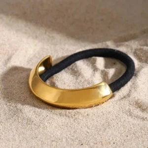 Gold crescent hair tie cuff shown at oblique angle on sandy beach backdrop, luxury minimalist design